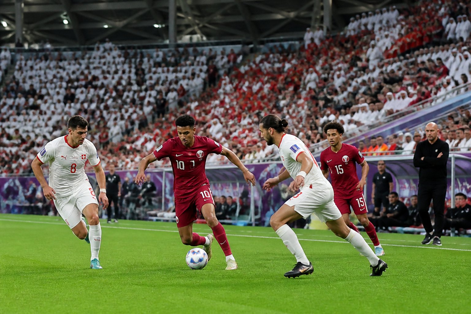 Katar ve İsviçre takımlarının maçında futbol sahasında oynayan oyuncular ve kenarda teknik direktörler.