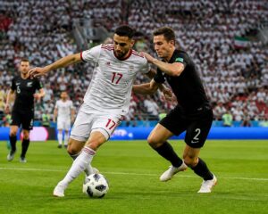 İran ve Yeni Zelanda milli takımları arasında bir Dünya Kupası maçında sahada mücadele eden iki futbolcu.