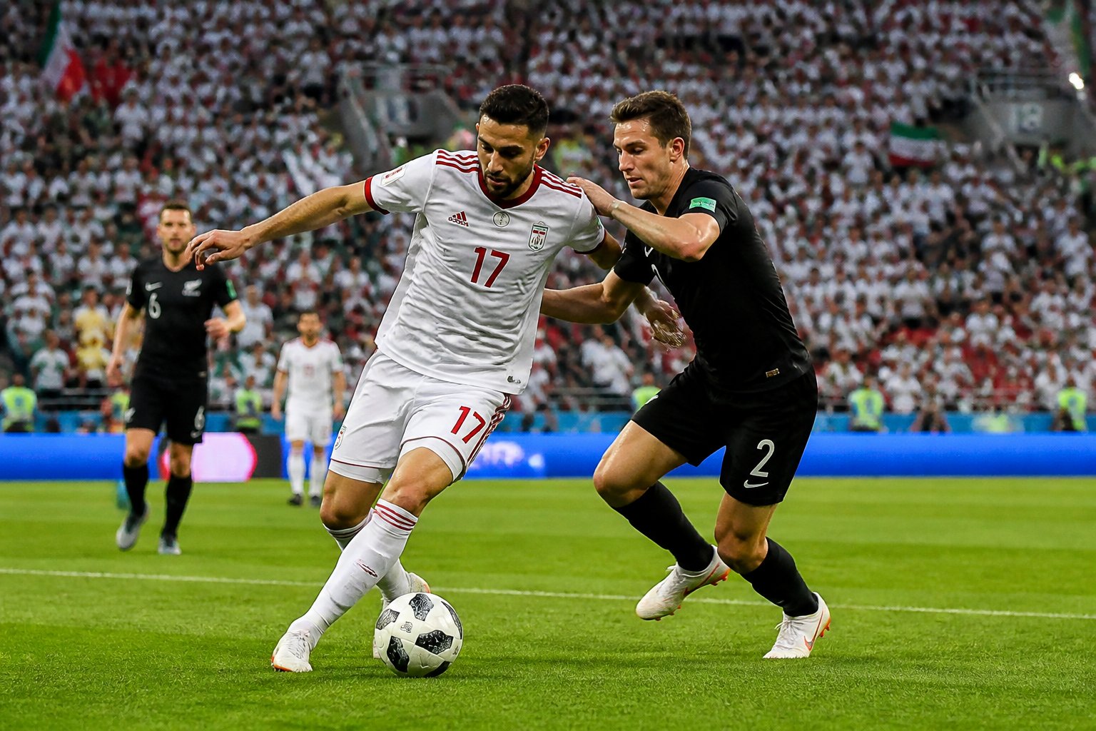 İran ve Yeni Zelanda milli takımları arasında bir Dünya Kupası maçında sahada mücadele eden iki futbolcu.