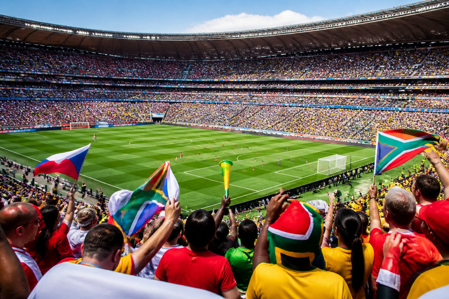 Çek Cumhuriyeti ile Güney Afrika arasında Dünya Kupası maçının oynandığı, dolu bir stadyum ve sahada futbolcuların mücadele ettiği bir sahne.
