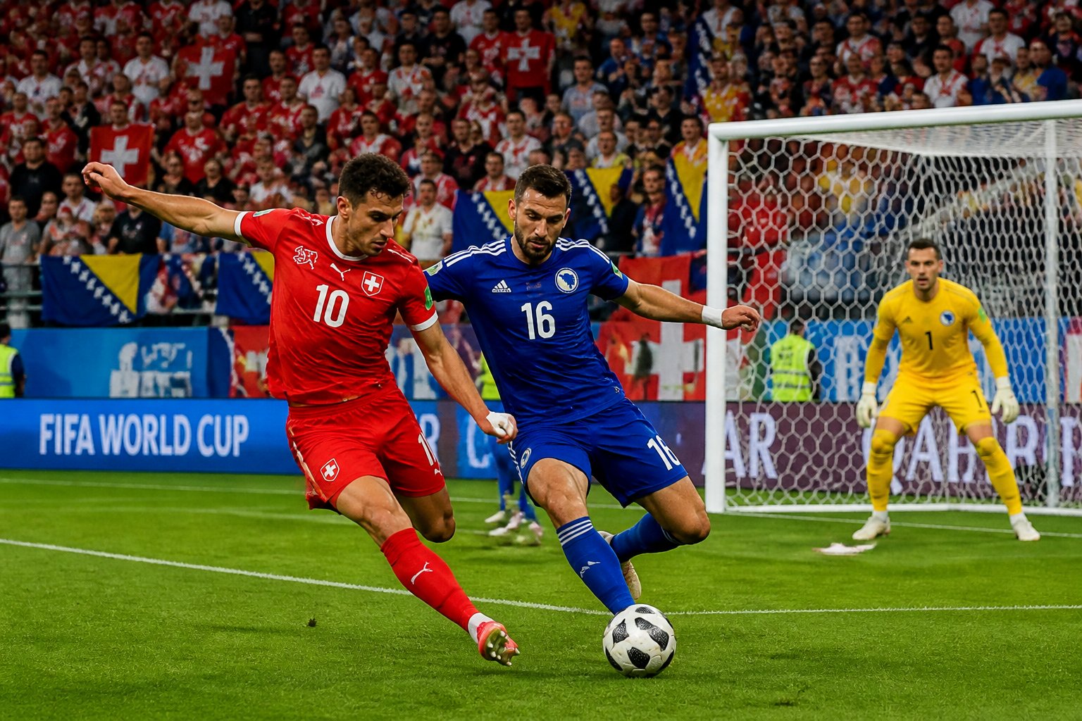 İsviçre ve Bosna Hersek takımları arasında Dünya Kupası maçında iki futbolcu top için mücadele ediyor, kalenin önünde yoğun bir atmosfer var.