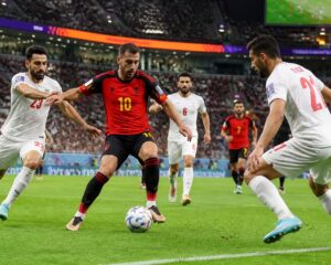 Belçika ve İran takımlarının büyük bir kalabalık önünde futbol maçı oynadığı sahne.