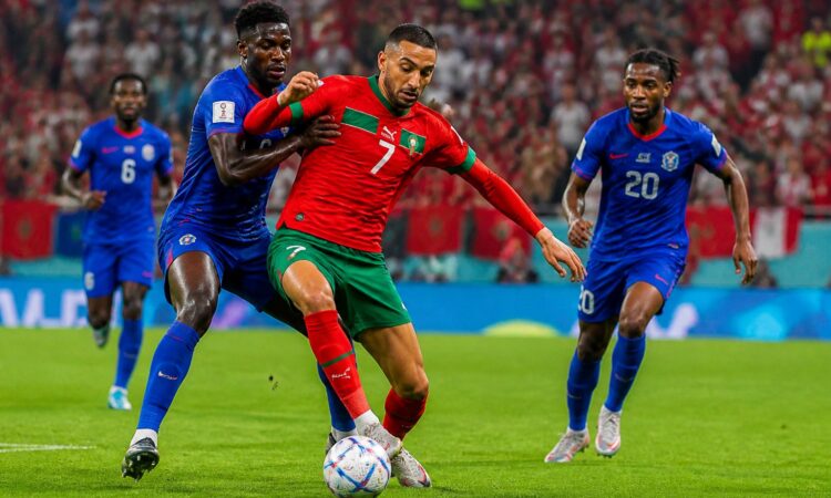 Fas ve Haiti takımları arasında Dünya Kupası maçında oyuncular top için mücadele ediyor, tribünlerde taraftarlar tezahürat yapıyor.