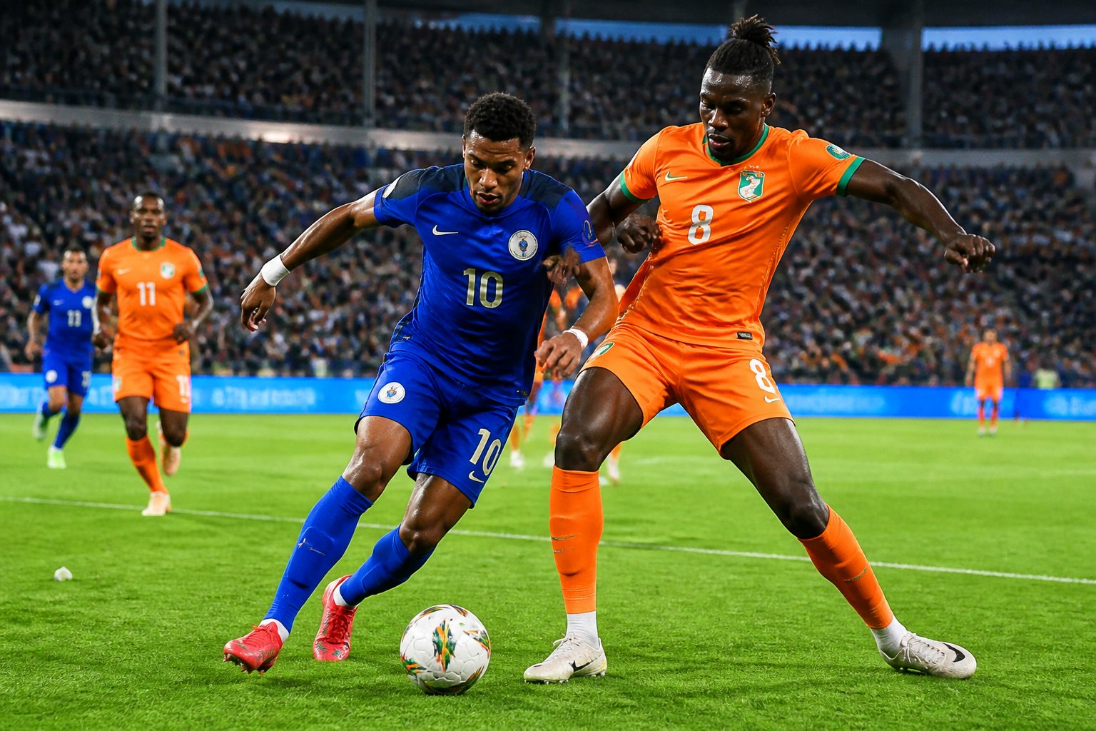 Curaçao ve Fildişi Sahili arasındaki Dünya Kupası maçında futbolcular sahada mücadele ediyor, tribünlerde taraftarlar yer alıyor.