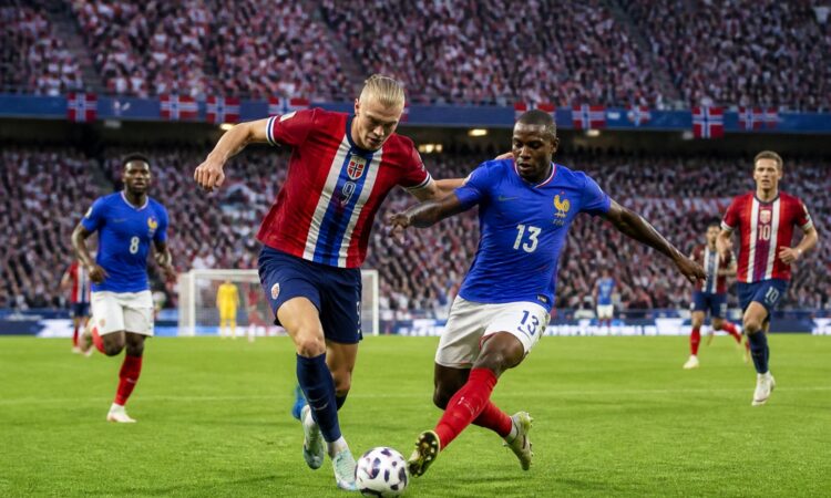 Norveç ve Fransa takımları arasında Dünya Kupası maçında futbolcular sahada mücadele ediyor, tribünler dolu ve seyirciler maçı izliyor.
