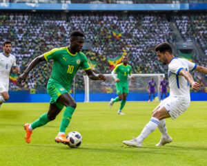 Senegal ve Irak arasında Dünya Kupası maçında sahada topa sahip olan oyuncular ve arka planda dolu tribünler.