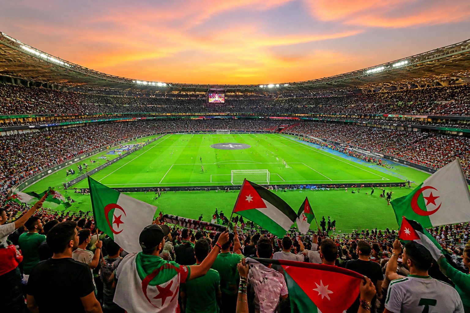 Ürdün ve Cezayir milli takımlarının maçına hazırlanan, dolu bir stadyumda futbol sahası ve taraftarlar.